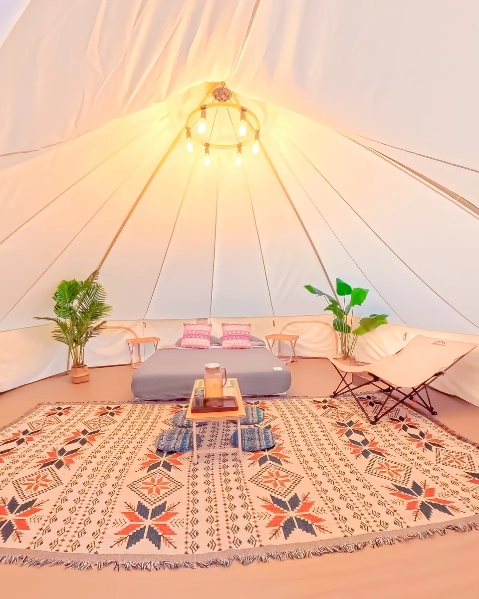 Lampu hiasan menyala di dalam bell tent dengan karpet corak